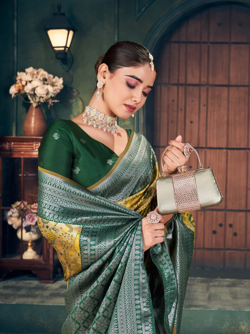 Woman in a green saree holding a handbag in an indoor setting
